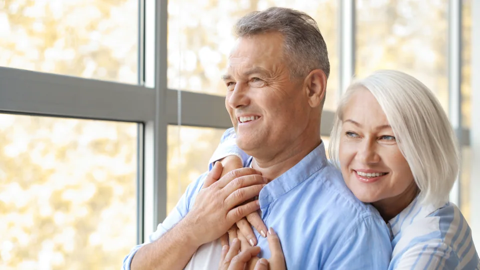 An older couple smiling together by a bright window